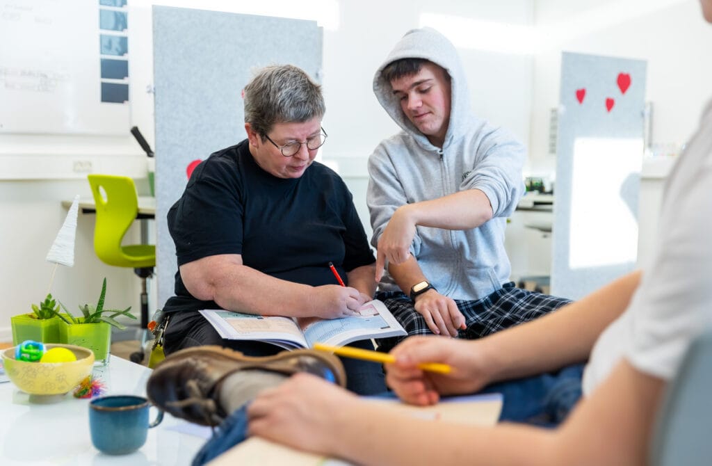 En elev og en lærer laver lektier, med en anden elev i forgrunden